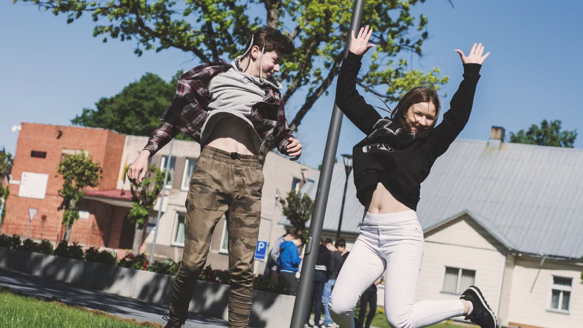 Two teenagers joyfully jumping outdoors in Šiluva, Lithuania under a bright blue sky. Captured in springtime.